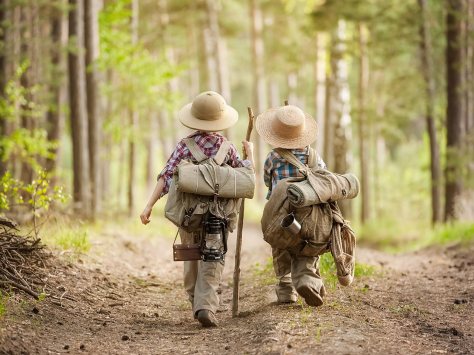 Two kids with backpacks exploring a forest, traveling the world